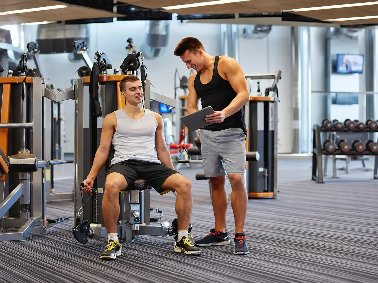 Gym trainer helping a member while using a tablet beside gym equipment